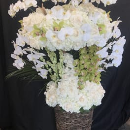 Tall white floral arrangement in a woven basket with arching orchids