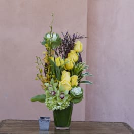 Tall yellow rose arrangement in a green vase with mixed blooms