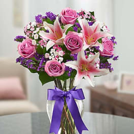 Pink roses and lilies in a glass vase with a purple ribbon