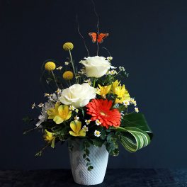 Mixed flower arrangement in a white vase with a butterfly accent