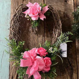 Two pink rose wreaths with ribbon accents on a rustic wood background