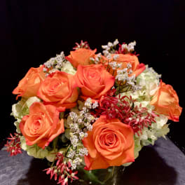 Orange roses arranged in a glass vase with white filler flowers