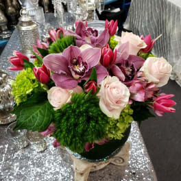 Pink orchids and roses arranged in a low vase with green accents