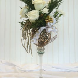 White roses arranged in a tall glass vase with gold ornaments and ribbon