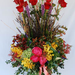 Tall arrangement of red roses, pink blooms, and yellow flowers in a striped vase
