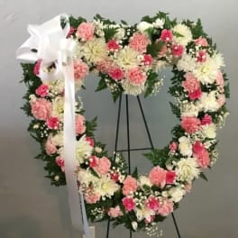 Heart-shaped floral wreath with pink and white flowers on a stand