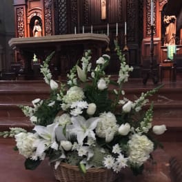 White floral arrangement in a wicker basket at an altar