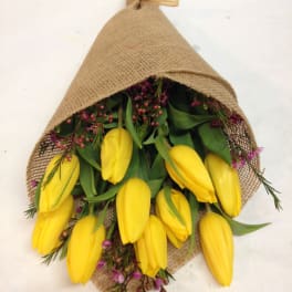 Bundle of yellow tulips wrapped in burlap with small purple flowers