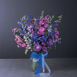 Bouquet of purple and blue flowers in a glass vase with ribbon
