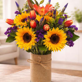 Bouquet of sunflowers, orange lilies, and purple filler in a glass vase