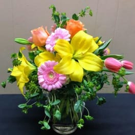 Bouquet of yellow lilies, pink gerbera daisies, and roses in a glass vase