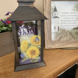 Decorative lantern with sunflower artwork and a memorial frame beside it