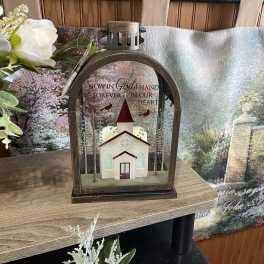 Memorial lantern with a church scene and white flowers beside it