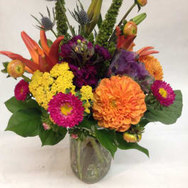 Bright mixed arrangement of orange, yellow, and pink flowers in a clear glass vase