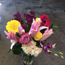 Mixed bouquet in a clear glass vase with pink lilies, roses, gerbera daisies, and purple blooms