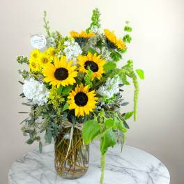 Sunflower arrangement in a glass vase with white blooms and green accents