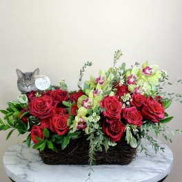 Red roses and green orchids in a woven basket with a cat figurine