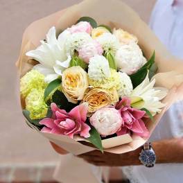 Hand-tied bouquet of white and pink lilies, roses, peonies, and mixed blooms wrapped in beige paper.