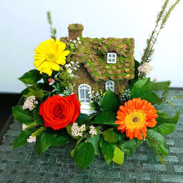 Miniature house surrounded by red, yellow, and orange flowers