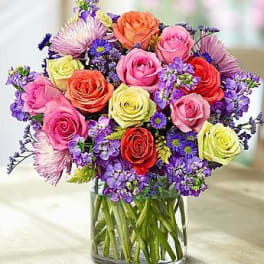 Mixed bouquet of roses and purple flowers in a glass vase