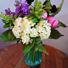 Mixed bouquet of white hydrangeas, purple blooms, and pink tulips in a blue vase