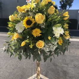 Yellow roses and mixed blooms arranged in a tall gold vase
