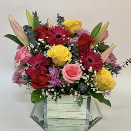 Mixed bouquet of roses, gerbera daisies, and lilies in a mirrored box vase