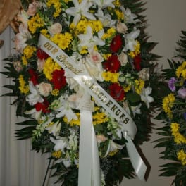 Large funeral wreath with white lilies, yellow daisies, and red flowers