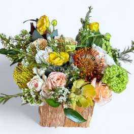 Mixed bouquet in a rustic wooden container with yellow, peach, white, and green blooms