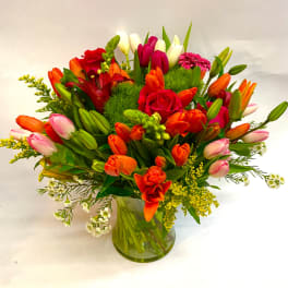 Mixed bouquet of tulips, roses, and a pink gerbera daisy in a glass vase