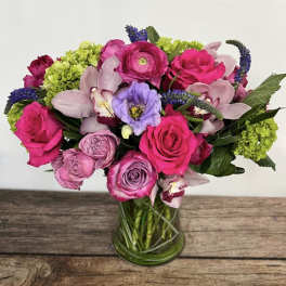 Bright pink and purple bouquet with roses, ranunculus, orchids, and hydrangea in a clear glass vase