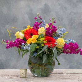 Mixed bouquet of roses, gerbera daisies, and purple blooms in a glass vase