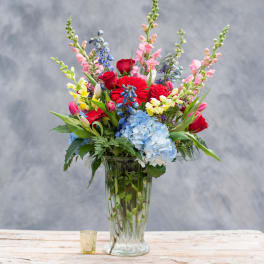 Mixed bouquet in a clear glass vase with red, pink, blue, and yellow flowers