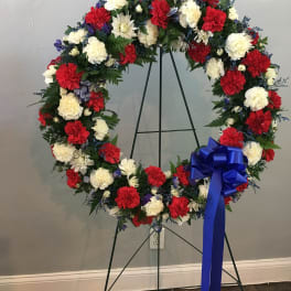 Circular wreath of red, white, and blue flowers on a stand with a blue bow