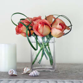 Pink roses in a clear glass vase with curled green ribbon