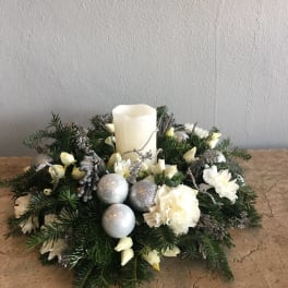 Holiday centerpiece with a white pillar candle, white flowers, and silver ornaments