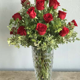 Red roses arranged in a tall glass vase with mixed greenery