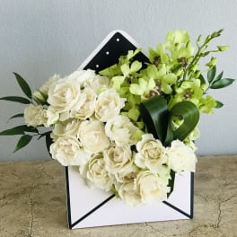White roses and green orchids arranged in a white envelope box