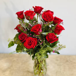 Red roses arranged in a clear glass vase with small pink filler flowers