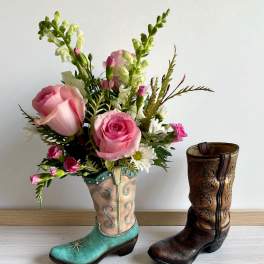 Pink rose bouquet arranged in a turquoise cowboy boot vase beside a brown boot