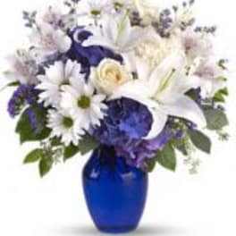 Mixed white and blue flower arrangement with lilies and daisies in a deep blue glass vase