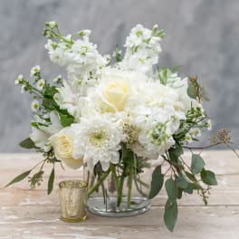 White floral arrangement in a clear glass vase with a small gold candle holder