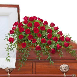 Red rose casket spray with trailing greenery on a wooden casket