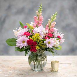 Pink and white mixed bouquet in a glass vase with a small candle holder beside it