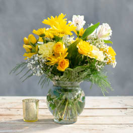Yellow and white bouquet in a clear glass vase with a small candle beside it