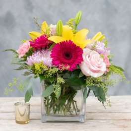 Pink and yellow mixed flower arrangement in a square glass vase