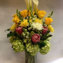 Mixed bouquet with yellow roses, white calla lilies, and pink protea in a glass vase