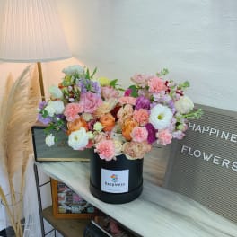Mixed pastel flower arrangement in a black hatbox beside a lamp