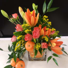 Orange lilies and pink roses in a glass vase with oranges