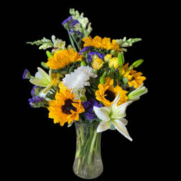 Bouquet of sunflowers, white lilies, and purple filler in a glass vase